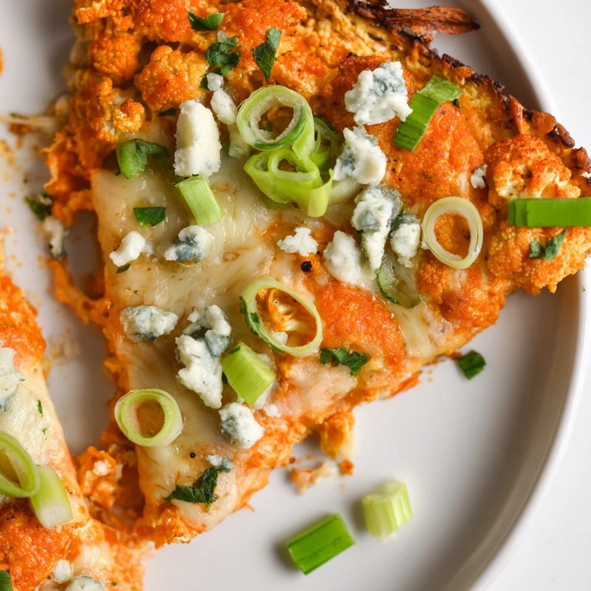 A close-up of Buffalo Cauliflower Pizza, featuring a cheesy, golden cauliflower crust topped with vibrant buffalo sauce and herbs.
