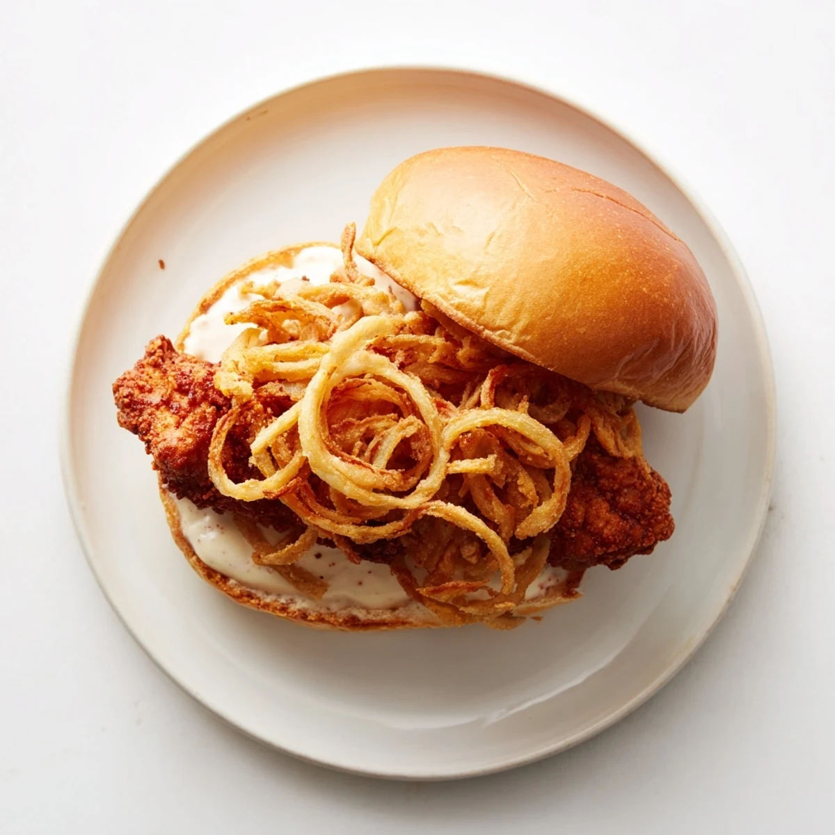 Golden fried chicken thigh layered on a soft brioche bun with crispy onion rings and creamy aioli.