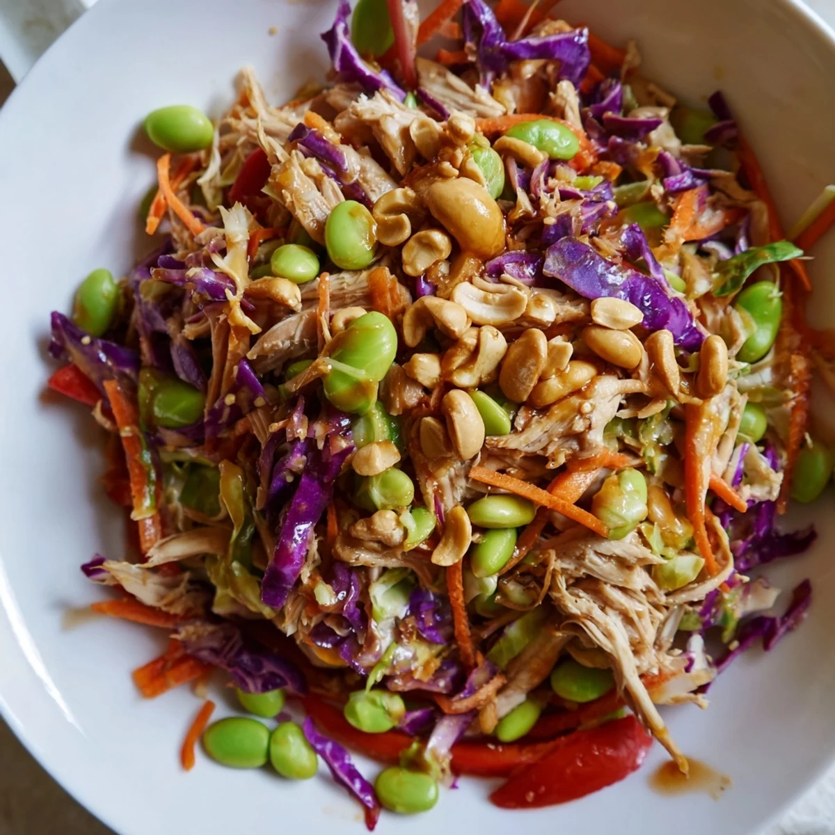 A vibrant bowl of Edamame Crunch Chicken Salad with shredded chicken, crisp cabbages, and colorful vegetables tossed in a zesty ginger dressing.