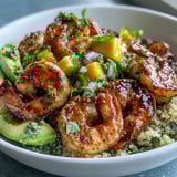 Tangy lime chili sauce coats smoky grilled shrimp beside creamy avocado and nutty quinoa in a bright bowl.