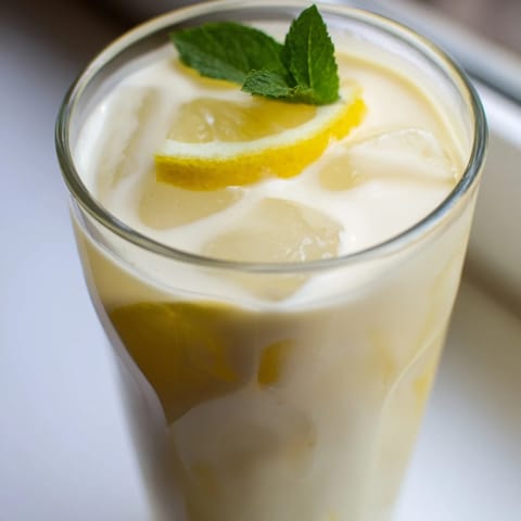 Overhead view of creamy lemonade drink in a tall glass with ice, lemon slices, and fresh mint.