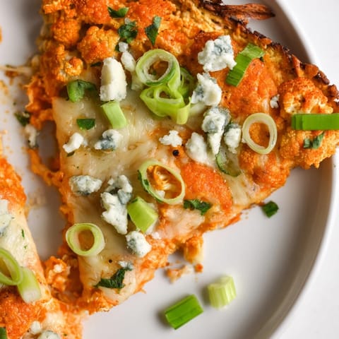 A close-up of Buffalo Cauliflower Pizza, featuring a cheesy, golden cauliflower crust topped with vibrant buffalo sauce and herbs.