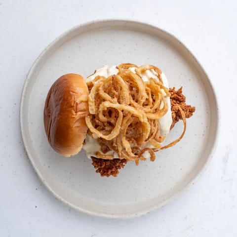 Close-up of a juicy Crispy Onion Chicken Sandwich with melted butter on toasted buns and fresh lettuce.