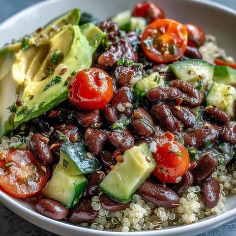 Hearty Three-Bean Power Bowl with mixed greens, diced cucumber, and red bell pepper, drizzled with a zesty lemon-herb dressing for a nutritious meal.