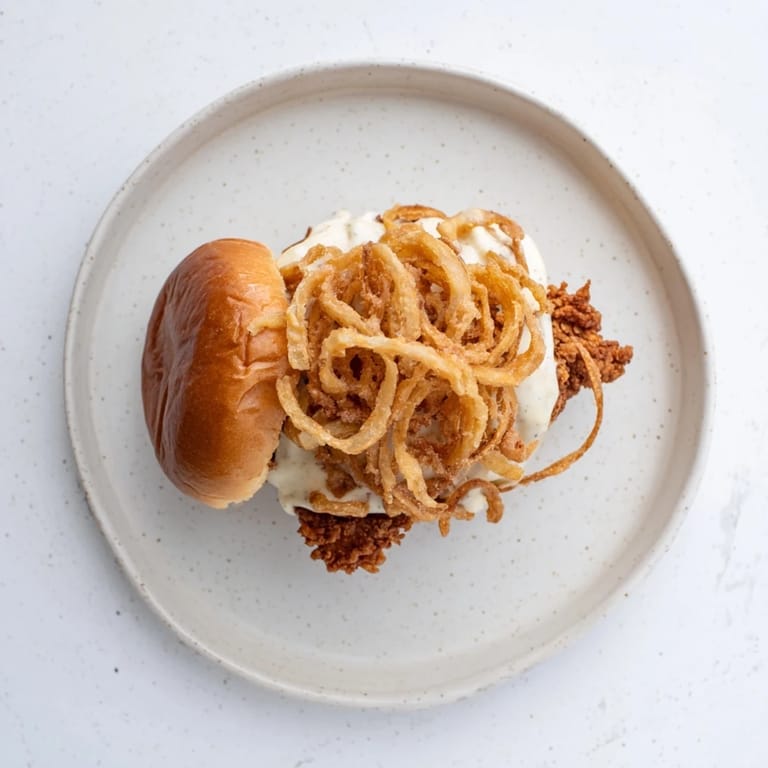Close-up of a juicy Crispy Onion Chicken Sandwich with melted butter on toasted buns and fresh lettuce.