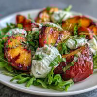 A colorful summer salad with grilled peaches, creamy burrata, and honey drizzle, served on fresh arugula.